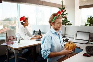 Regalos de navidad para empresas. Un par de personas en una oficina con adornos de navidad sujetan sus regalos de empresas sobre sus escritorios.