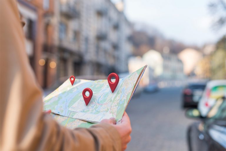 crear la ficha de Google My Business. Una mujer sujeta un mapa del que salen 3 pines de sitio en 3D